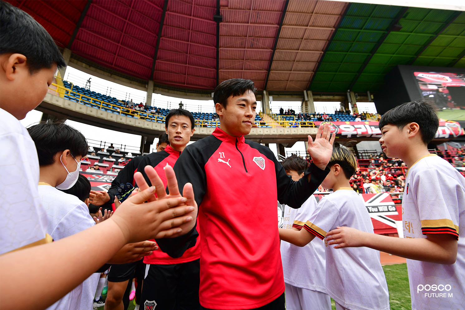 축구교실에 참여한 어린이들이 (앞쪽부터) 포항스틸러스 정재희, 김종우 선수와 하이파이브를 나누며 즐거워하고 있다. 이날 정재희 선수는 후반 48분 &lsquo;극장 결승골&rsquo;을 기록하며 팀을 승리로 이끌었다.