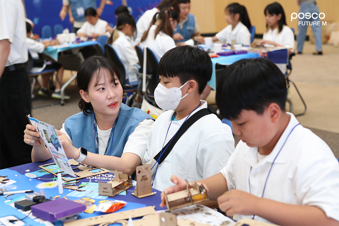 포스코퓨처엠 직원이 푸른꿈 환경캠프에 멘토로 나서 어린이와 함께 전기차 모형을 제작하고 있다