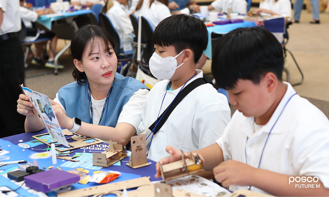 포스코퓨처엠 직원이 푸른꿈 환경캠프에 멘토로 나서 어린이와 함께 전기차 모형을 제작하고 있다